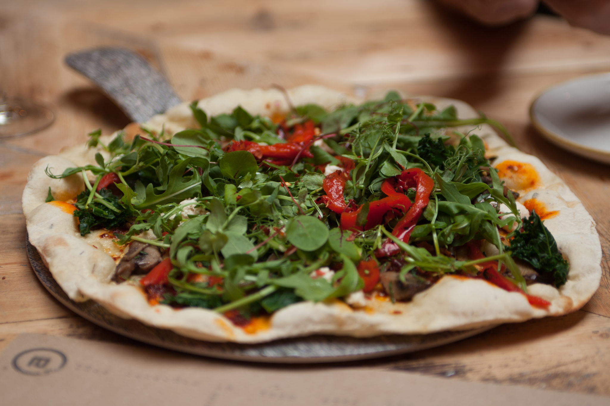 Flatbread topped with leafy greens, red peppers and vegetables