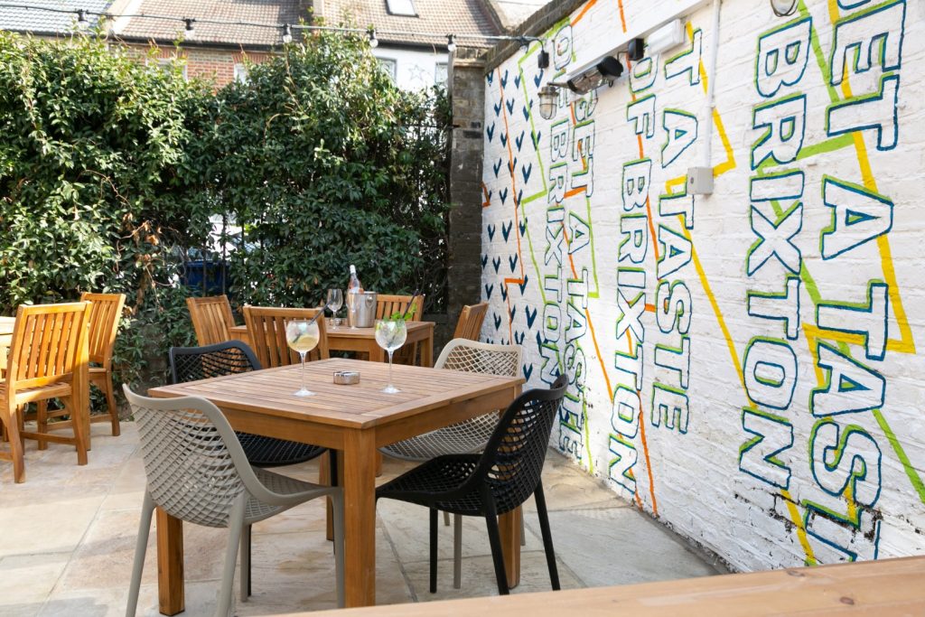 Garden tables and chairs beside a colourful Brixton Brewery mural
