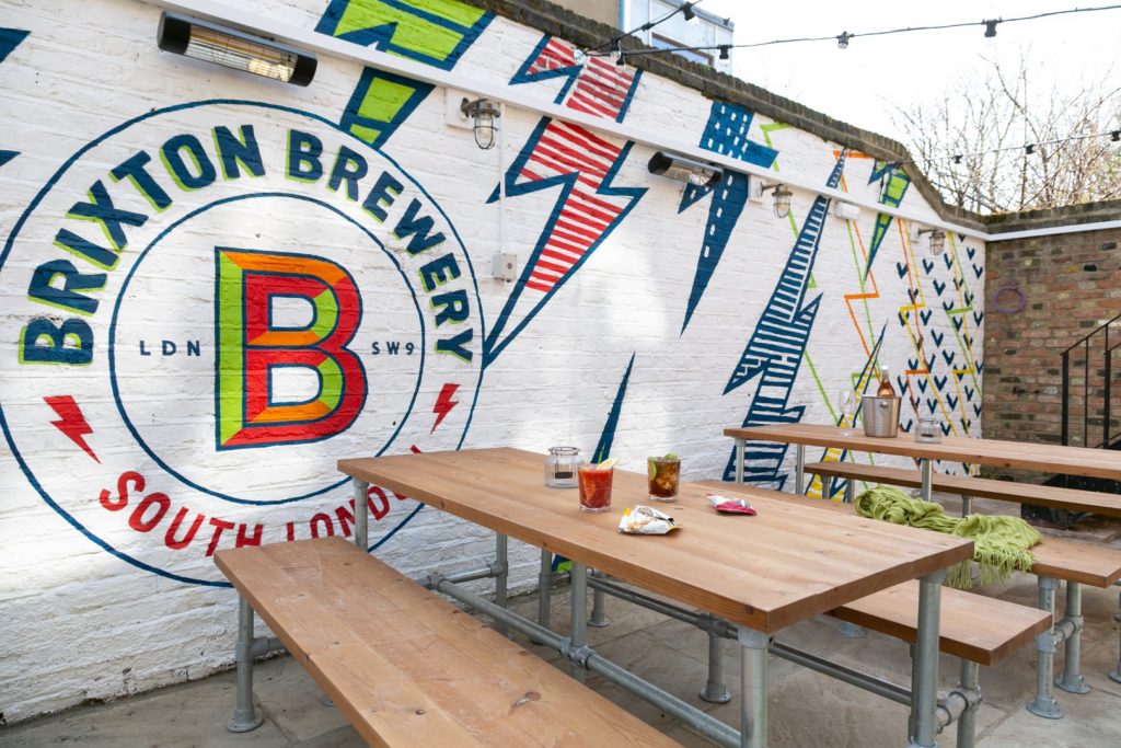 Brixton Brewery mural beside wooden benches in The Cambria garden