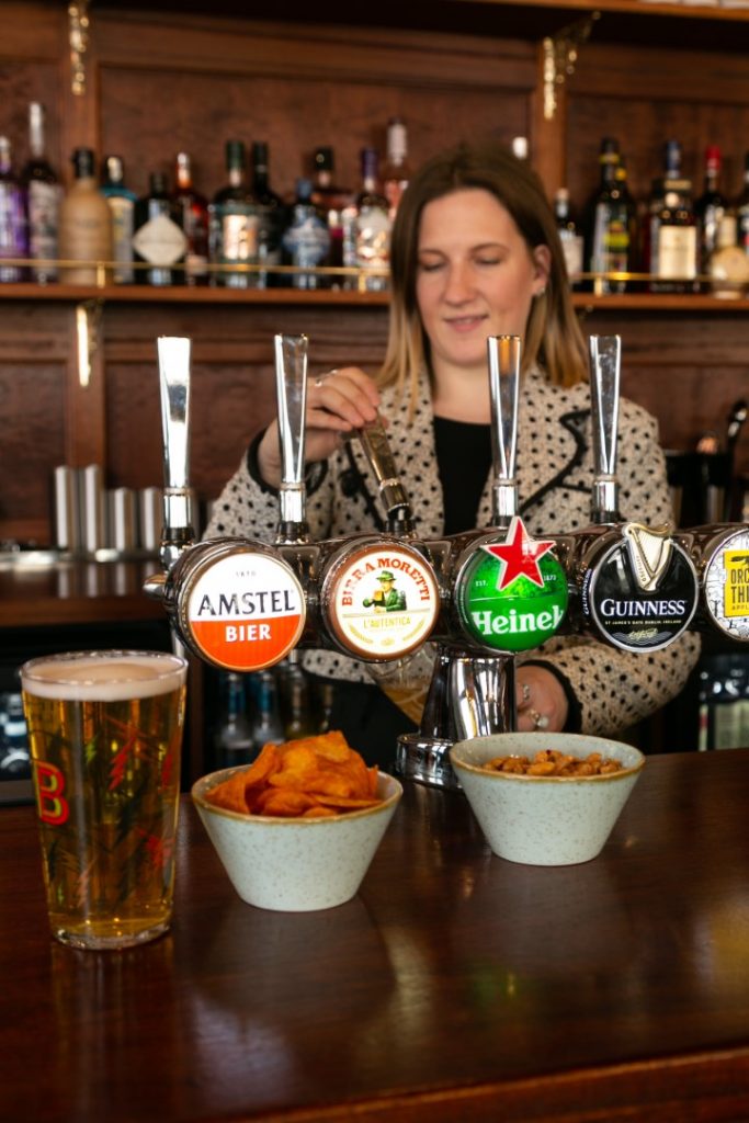 Bartender behind beer taps with a pint and bowls of bar snacks