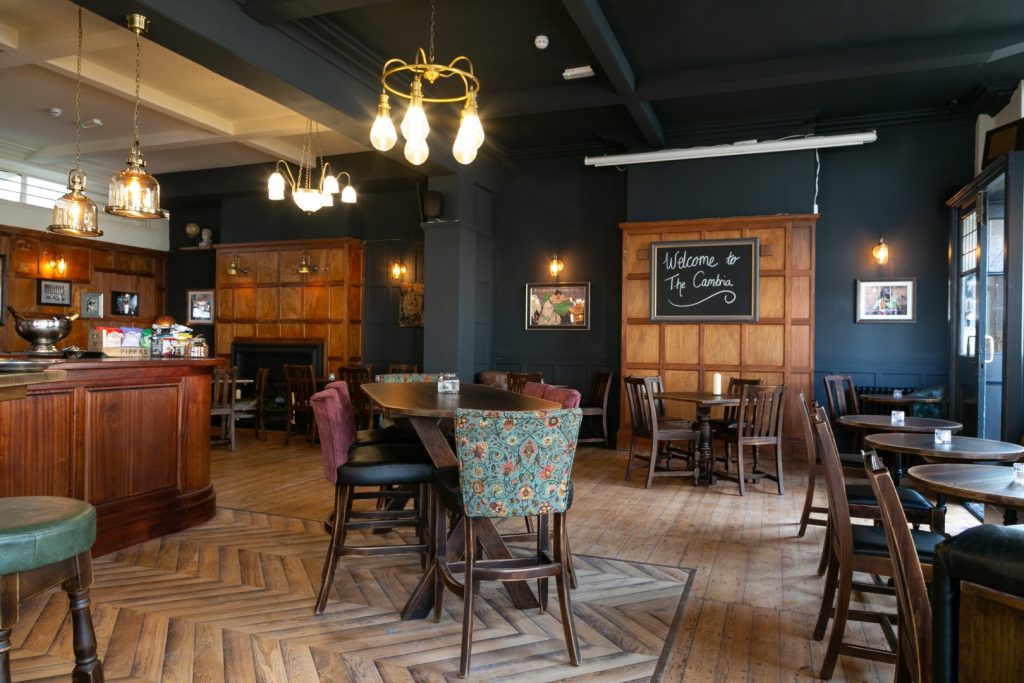 The Cambria pub interior with wooden tables, chairs, bar and warm hanging lights
