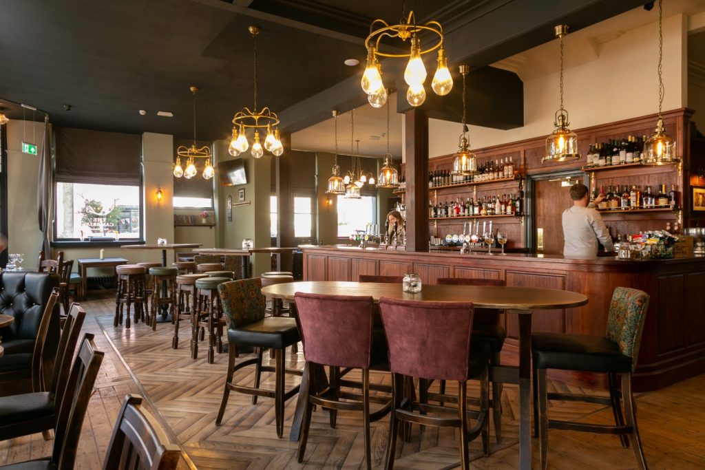 The Cambria pub interior with wooden tables, chairs, bar and hanging lights