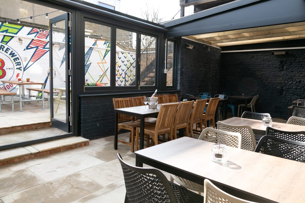 Covered garden seating area with wooden tables, chairs and a colourful mural outside