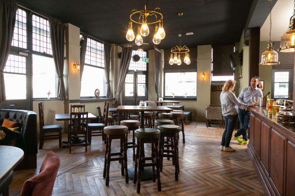 Bright pub interior with tables, stools and guests standing at the bar