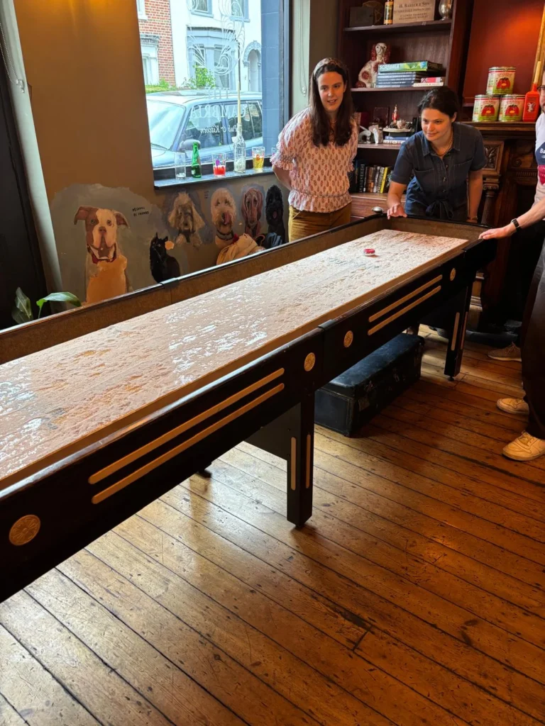 Guests standing at the end of a long wooden shuffleboard table