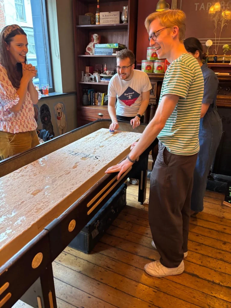 Guests smiling and playing together around a shuffleboard table