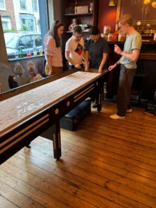 Four people gathered around the shuffleboard table at The Cambria